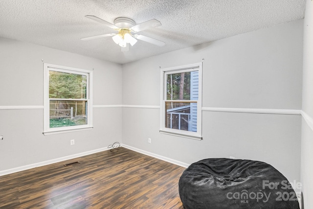 living area featuring dark wood-type flooring, ceiling fan, plenty of natural light, and a textured ceiling