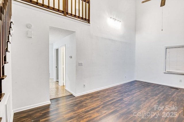 unfurnished living room with a high ceiling, dark hardwood / wood-style floors, and ceiling fan