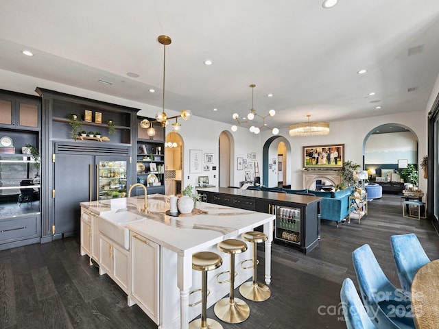 kitchen with sink, a kitchen bar, hanging light fixtures, a kitchen island with sink, and light stone countertops