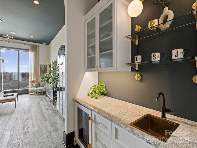 kitchen with white cabinetry, beverage cooler, light stone countertops, and sink