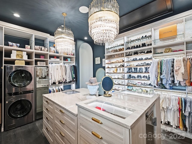 spacious closet featuring dark wood-type flooring, stacked washer / drying machine, and a notable chandelier