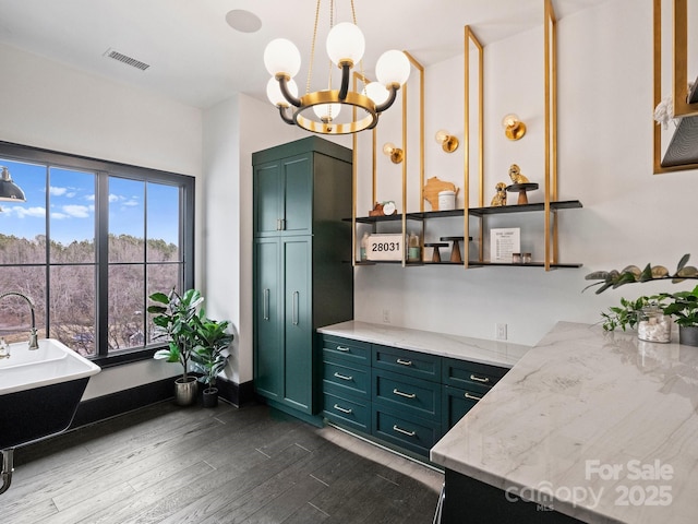 interior space with an inviting chandelier, decorative light fixtures, green cabinets, light stone countertops, and hardwood / wood-style floors