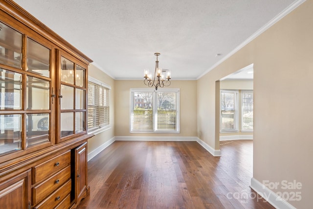 unfurnished dining area featuring ornamental molding, plenty of natural light, dark wood-type flooring, and a notable chandelier