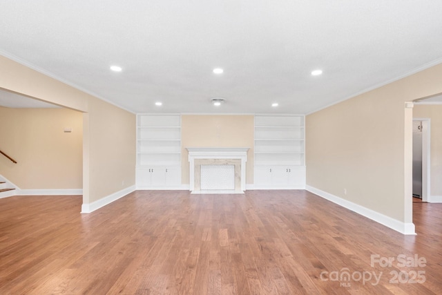 unfurnished living room with a premium fireplace, crown molding, built in features, and light wood-type flooring