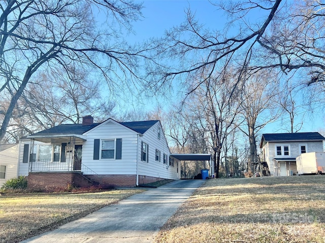 view of side of property featuring driveway, a lawn, a chimney, an attached carport, and a porch