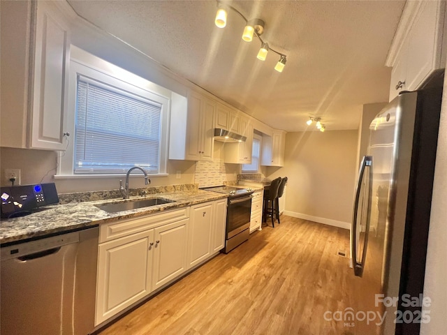 kitchen featuring stainless steel appliances, light wood-style floors, white cabinets, a sink, and under cabinet range hood