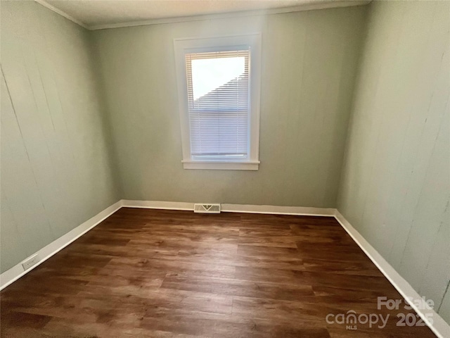 empty room featuring crown molding, dark wood-type flooring, visible vents, and baseboards