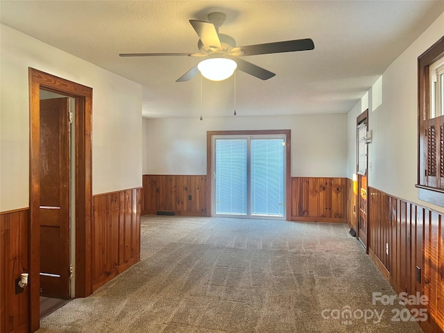 carpeted empty room with ceiling fan, a textured ceiling, and wooden walls