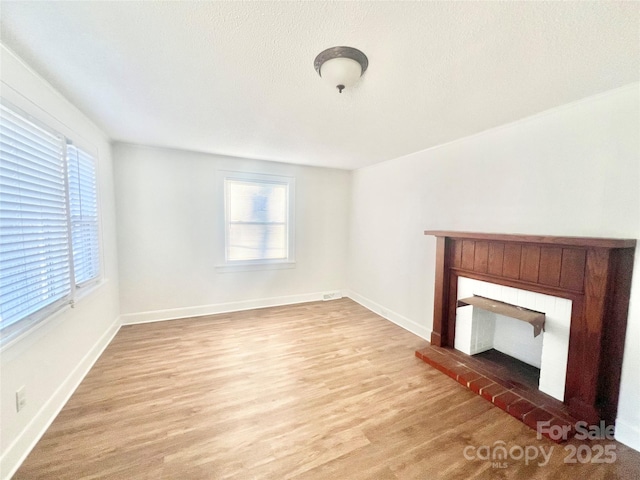 unfurnished living room featuring light wood-style floors, plenty of natural light, a fireplace, and baseboards