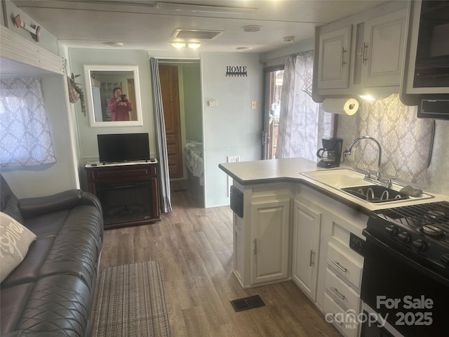 kitchen with hardwood / wood-style floors, sink, white cabinets, decorative backsplash, and black gas stove