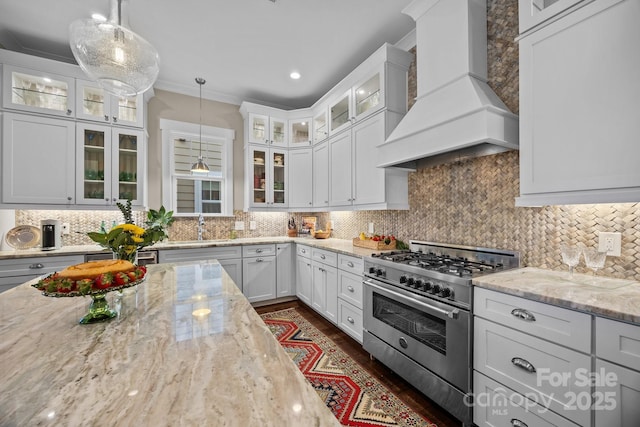 kitchen featuring custom exhaust hood, light stone counters, white cabinetry, hanging light fixtures, and stainless steel range