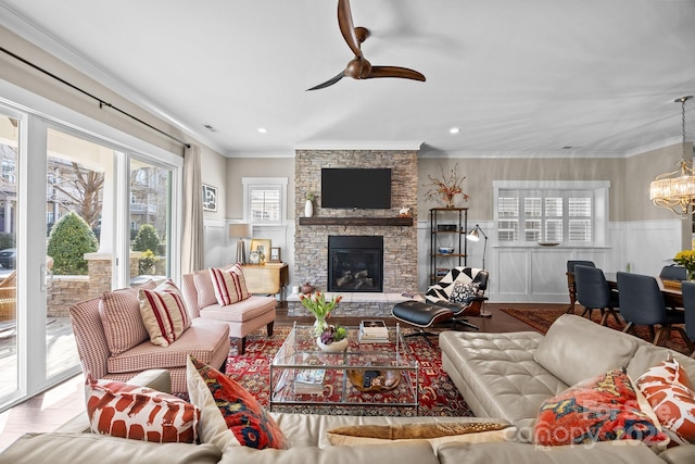 living room featuring a stone fireplace, ceiling fan with notable chandelier, ornamental molding, and hardwood / wood-style flooring