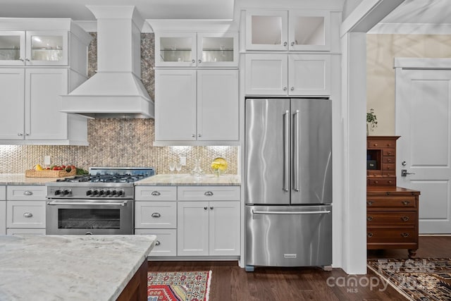 kitchen with dark wood-type flooring, premium range hood, white cabinetry, high quality appliances, and light stone countertops