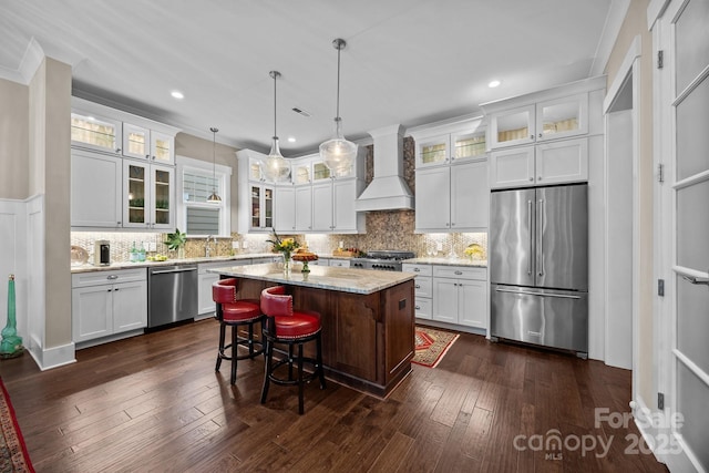 kitchen with a kitchen bar, custom exhaust hood, decorative light fixtures, a kitchen island, and stainless steel appliances