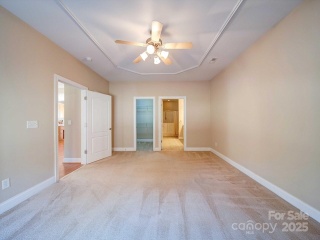 unfurnished bedroom featuring ensuite bathroom, a walk in closet, light carpet, and ceiling fan