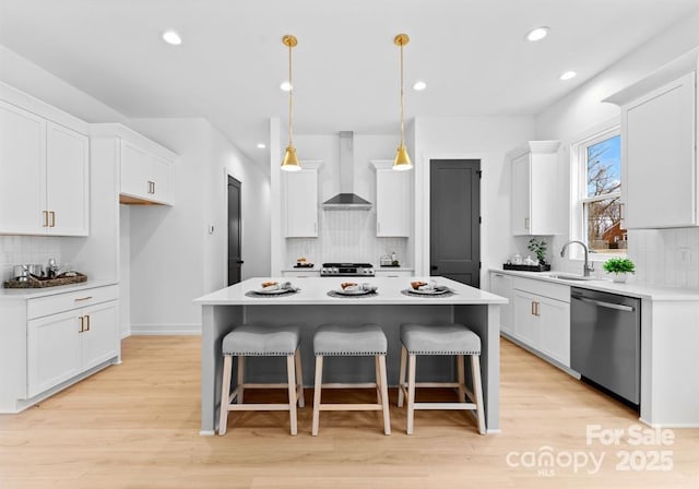 kitchen with white cabinetry, a kitchen island, stainless steel dishwasher, and wall chimney range hood