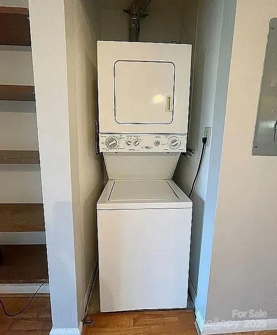 clothes washing area with hardwood / wood-style flooring, electric panel, and stacked washer and clothes dryer