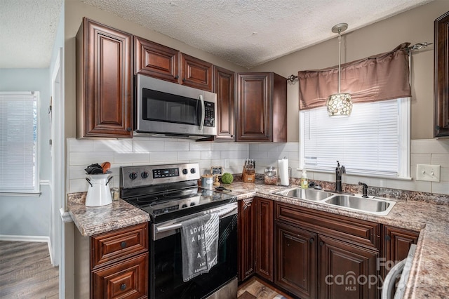 kitchen featuring sink, appliances with stainless steel finishes, hanging light fixtures, tasteful backsplash, and light stone countertops