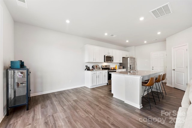 kitchen with a kitchen bar, white cabinetry, appliances with stainless steel finishes, an island with sink, and light stone countertops