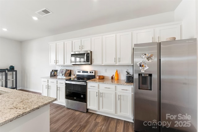 kitchen with appliances with stainless steel finishes, tasteful backsplash, white cabinets, light stone countertops, and dark wood-type flooring