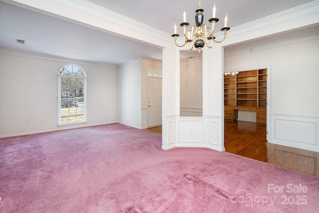 carpeted spare room featuring an inviting chandelier, built in desk, and ornamental molding