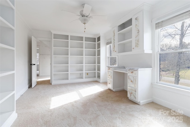 spacious closet featuring ceiling fan, light colored carpet, and built in desk