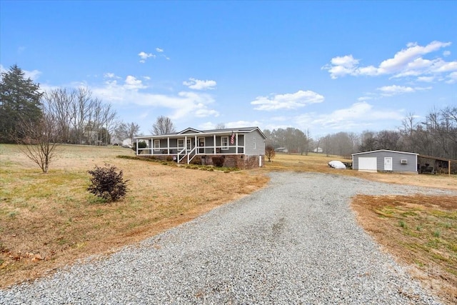 view of front of house with a front yard, a sunroom, covered porch, a garage, and an outdoor structure