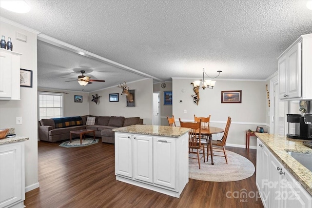 kitchen with ornamental molding, a center island, light stone countertops, and white cabinets