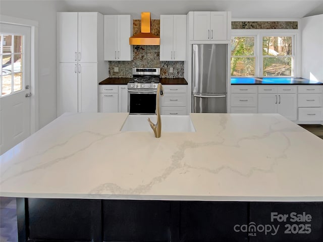 kitchen featuring wall chimney exhaust hood, sink, white cabinetry, stainless steel appliances, and a large island