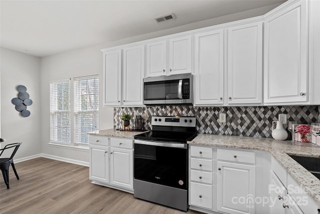 kitchen with white cabinetry, backsplash, stainless steel appliances, and light wood-type flooring