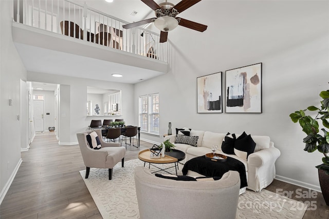 living room featuring ceiling fan, a towering ceiling, and wood-type flooring