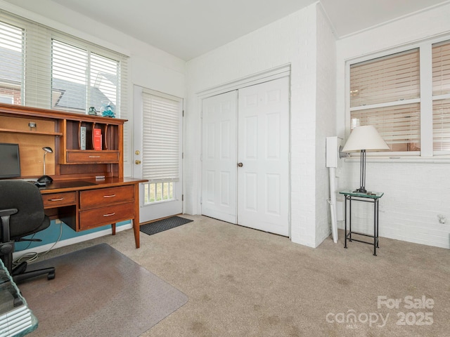 home office with light colored carpet, a healthy amount of sunlight, and brick wall