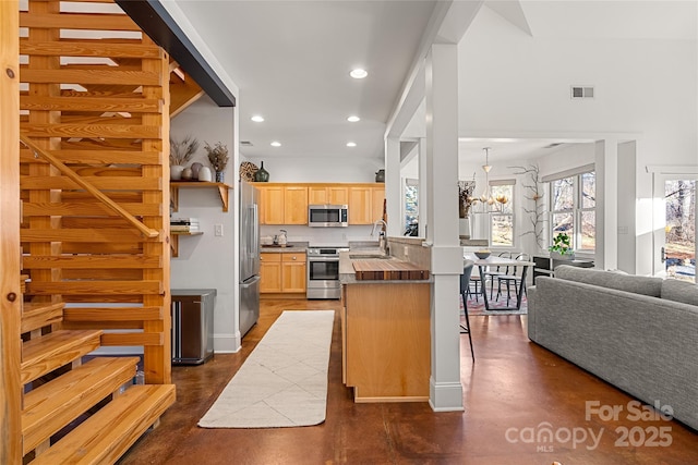 kitchen with light brown cabinetry, sink, appliances with stainless steel finishes, kitchen peninsula, and a notable chandelier