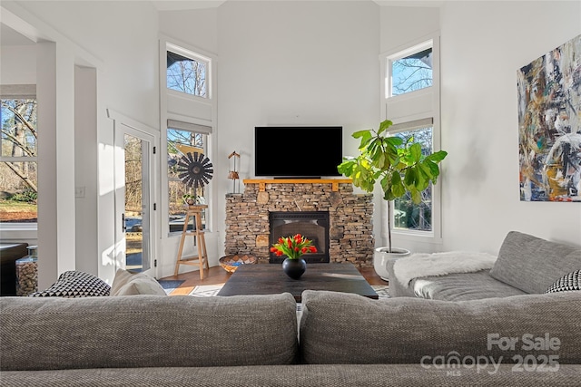 living room featuring hardwood / wood-style flooring, a stone fireplace, and a towering ceiling