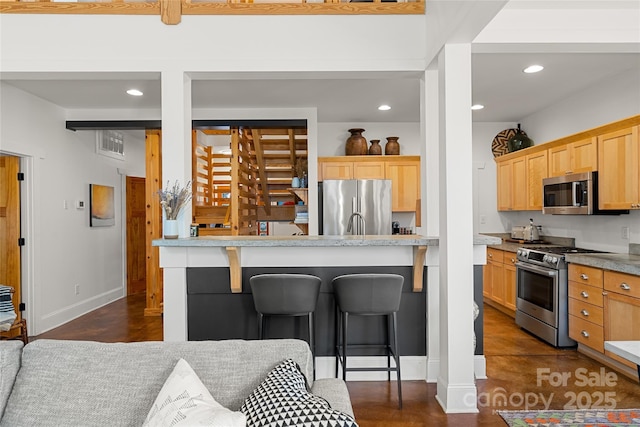 kitchen featuring appliances with stainless steel finishes, a breakfast bar area, light stone counters, and light brown cabinetry