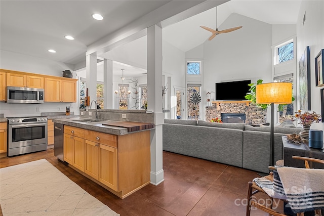 kitchen featuring sink, appliances with stainless steel finishes, high vaulted ceiling, a fireplace, and light brown cabinetry