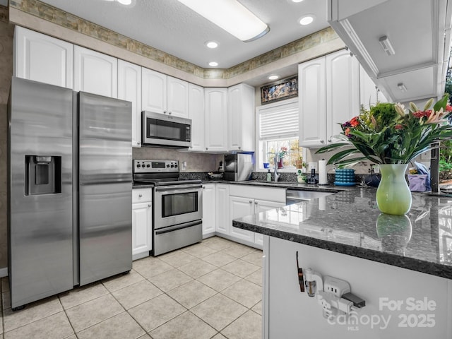 kitchen with white cabinetry, appliances with stainless steel finishes, dark stone countertops, and light tile patterned floors