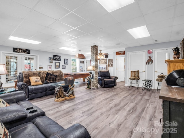 living room with a drop ceiling, french doors, and light wood-type flooring