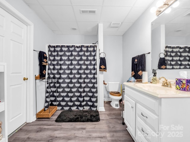 bathroom featuring a paneled ceiling, curtained shower, hardwood / wood-style flooring, vanity, and toilet