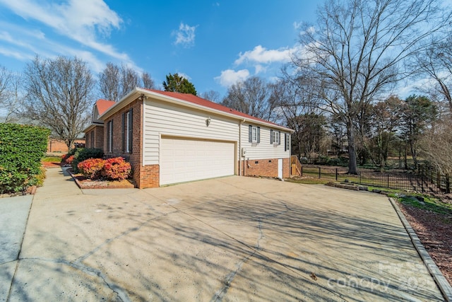 view of side of home featuring brick siding, fence, concrete driveway, a chimney, and an attached garage