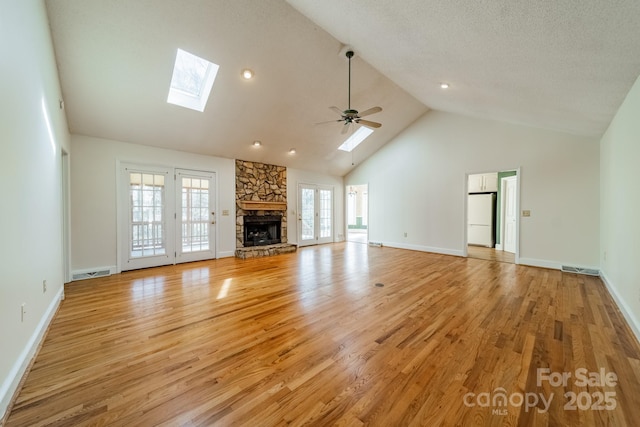 unfurnished living room featuring visible vents, high vaulted ceiling, a skylight, a stone fireplace, and light wood-style floors