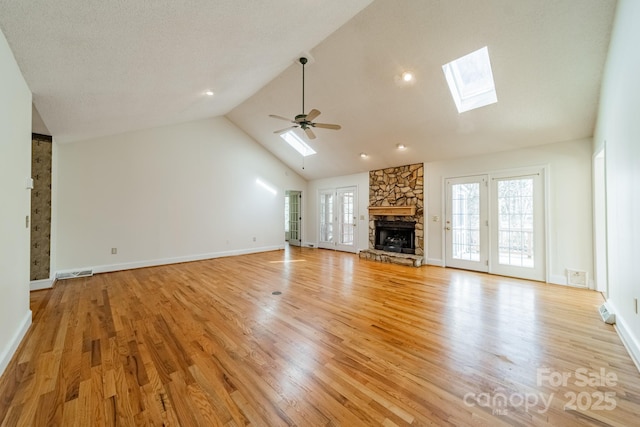 unfurnished living room with visible vents, light wood finished floors, a skylight, a fireplace, and ceiling fan