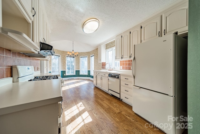 kitchen featuring light wood finished floors, a textured ceiling, white appliances, wallpapered walls, and light countertops