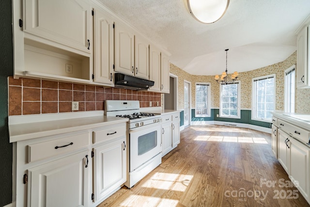 kitchen with wallpapered walls, light countertops, white gas range oven, and under cabinet range hood