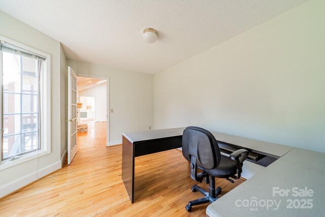 home office with a wealth of natural light, baseboards, light wood-style floors, and a textured ceiling