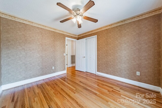 spare room with wallpapered walls, crown molding, wood finished floors, and baseboards