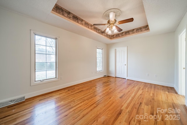 unfurnished bedroom with a tray ceiling, light wood-style flooring, baseboards, and visible vents