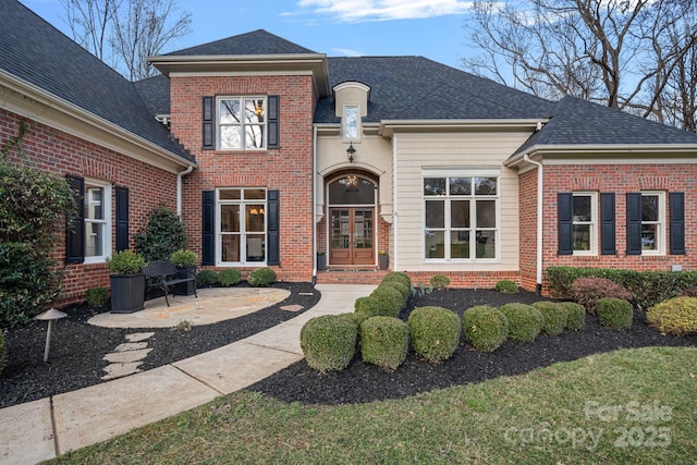 view of front facade with a patio area, brick siding, french doors, and roof with shingles