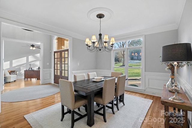 dining area featuring a chandelier, a wainscoted wall, crown molding, and wood finished floors