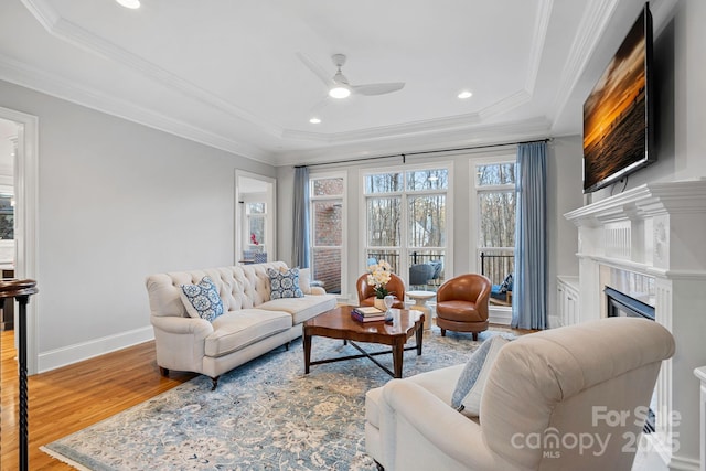 living room with a fireplace, crown molding, baseboards, and wood finished floors